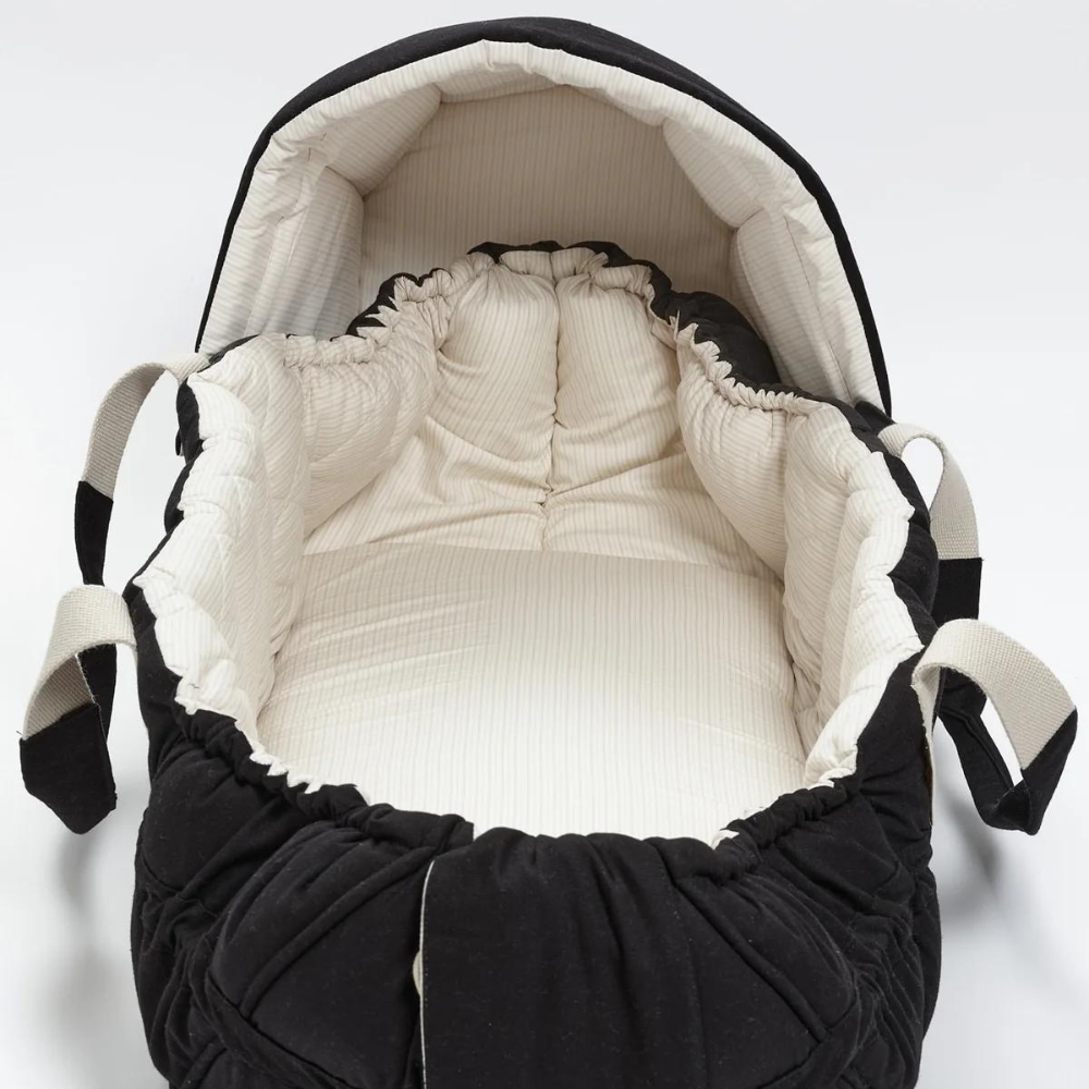 En sort Copenhagen Multifunktionel Kaleche til Babylift Black Solid m. Creme Stripe med cremefarvet indvendig polstring lavet af økologisk bomuld og to beige håndtag på hver side, lavet af genanvendt polyester, er vist mod en almindelig hvid baggrund. Kummen er ubesat, og dens quiltede sider fremstår bløde og polstrede for komfort af COPENHAGEN COLORS.